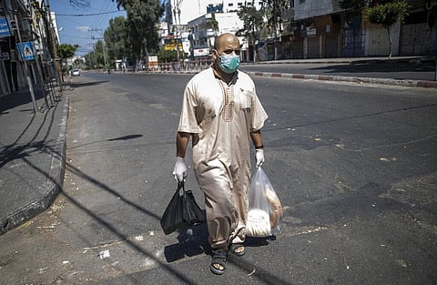 A Palestinian man wears a face mask and gloves carries his shopping during a lockdown imposed following the discovery of coronavirus cases in the Gaza Strip. (Photo | AP)