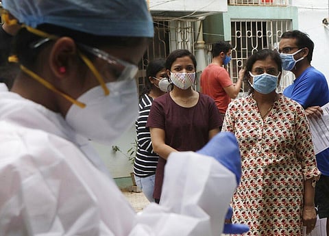 People watch as health workers take swab sample to test for COVID-19 outside a residential building in Mumbai, India, Sunday, Sept. 13, 2020. (Photo | AP)