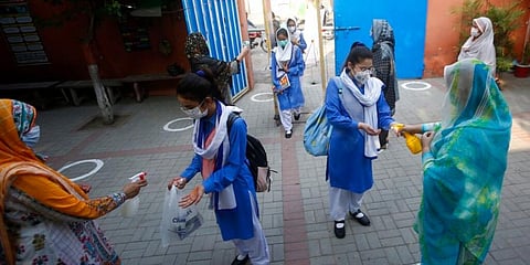 Teachers disinfect hands of students upon their arrival at a school, in Lahore, Pakistan. (Photo | AP)