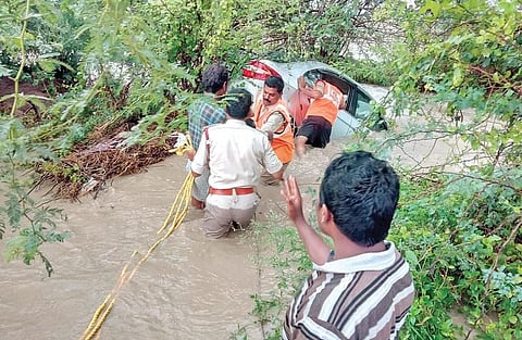 Fire and police department officials rescue two persons trapped in a car during flash floods at Banaganapalle on Saturday. (Photo | EPS)