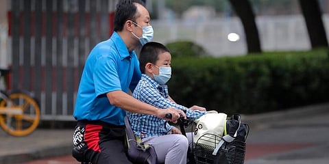 A man and a child wearing face masks ride on a bicycle past a street in China. (Photo | AP)