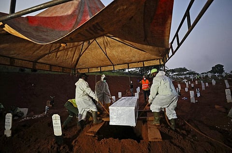 Workers lower a coffin containing the body of a suspected COVID-19 victim into a grave during a burial (Photo | AP)