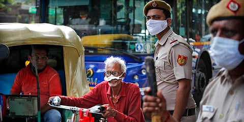 Delhi cops wearing masks stand at a traffic intersection as an elderly man pushes his cycle through a traffic jam. (Photo | AP)