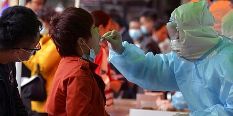 A medical staff takes a swab from a woman as residents line up for the COVID-19 test near the residential area in Qingdao in east China's Shandong province. (File Photo | AP)