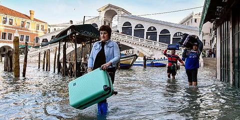 FILE - In this Monday, Dec. 23, 2019 file photo, people carry their luggage as they wade through water during a high tide of 1.44 meters near the Rialto Bridge, in Venice, Italy. (Photo | AP)