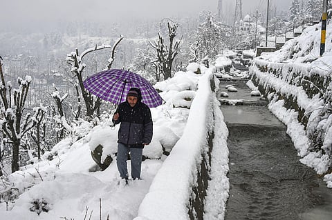 A man walks on a snow-covered path to climb up hill during snowfall on the outskirts of Srinagar (File Photo | PTI)