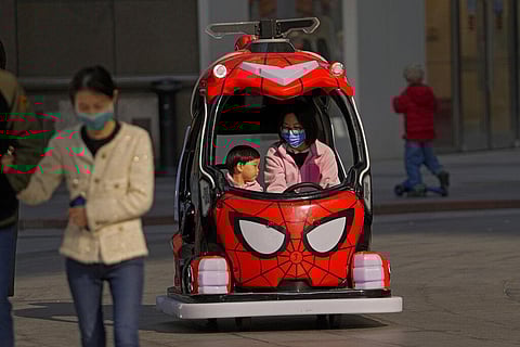 A woman wearing a face mask to help protect from the coronavirus rides on a toy car with a child at a shopping mall in Beijing, Sunday, Oct. 24, 2021. (Photo | AP)