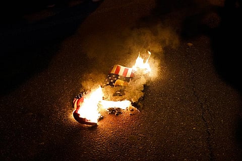 In this Nov. 14, 2020, file photo, a sign that counter-protesters lit on fire burns after supporters of President Donald Trump held pro-Trump marches Saturday, in Washington