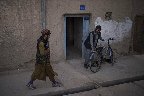 A man looks as a Taliban fighter patrols a neighborhood in search of a man accused in a stabbing incident, in Kabul. (Photo | AP)