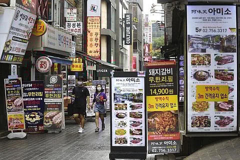People wearing face masks to help protect against the spread of the coronavirus pass by banners showing the menu items of restaurants in Seoul, South Korea (Photo | AP)