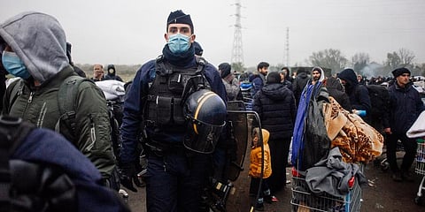 A police officer looks on as migrants gather in a camp in Grande-Synthe, Northern France. (Photo | AP)