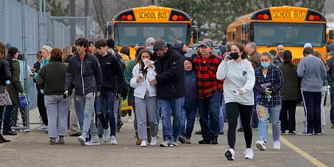 Parents walk away with their kids from the Meijer's parking lot, where many students gathered following an active shooter situation at Oxford High School. (Photo | AP)