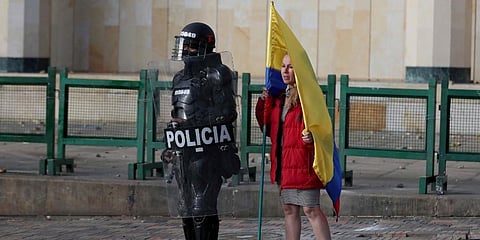 A woman holding a Colombian flag stands next to a police officer in riot gear during a protest in Bogota, Colombia. (Photo | AP)