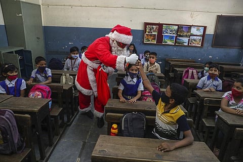 A man dress as Santa Claus greets students with a fist bump as they prepare to attend classes at a school in Mumbai. (Photo | AP)
