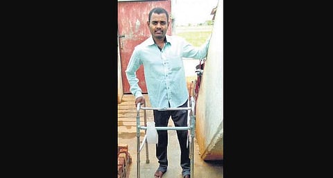 Adaikkalam Anandhan standing up for a moment using an assistive device, for a photo.