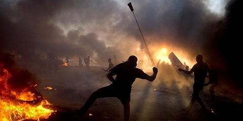 Black smoke from burning tires hangs in the sky as Palestinian protesters hurl stones toward Israeli troops during a protest at the Gaza Strip's border with Israel. (Photo | AP)