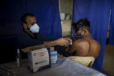 An Indian health worker administers the Covishield vaccine for COVID-19 to a construction worker at a bus stand in New Delhi. (Photo | AP)