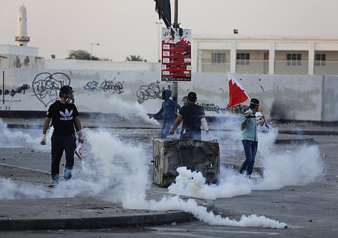 In this 2015 file photo, Bahraini anti-government protesters, one holding a national flag, clash with riot police firing tear gas in a suburb of Manama, Bahrain.