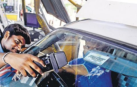 A tollgate employee scans a FASTag of a car.