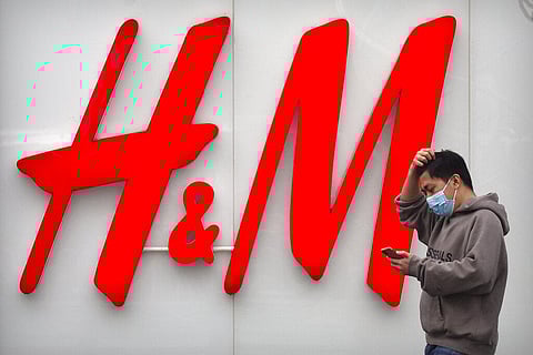 A man uses his smartphone as he walks past an H&M clothing store at a shopping mall in Beijing, Friday, March 26, 2021. (Photo | AP)