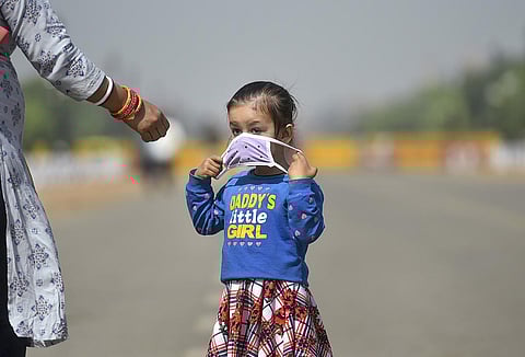A girl wearing a protective mask walks near the India Gate, in New Delhi. (Photo | PTI)