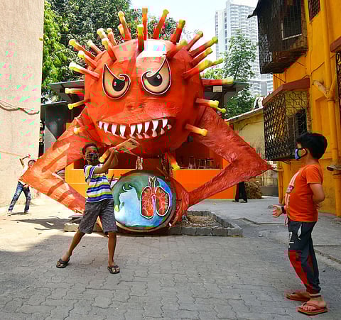 Children play near a giant demon to create awareness of COVID-19 on the eve of the Holi festival, in Mumbai on Sunday. (Photo | ANI)