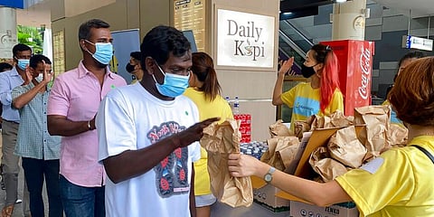 Migrant workers line up to receive gift bags from volunteers of the ItsRainingRaincoats at the Singapore Flyer Ferris Wheel attraction. (Photo | AP)