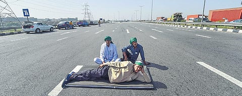 Farmers relax in the middle of the road during their blockade of the KMP Expressway in Ghaziabad on Saturday. (Photo | PTI)