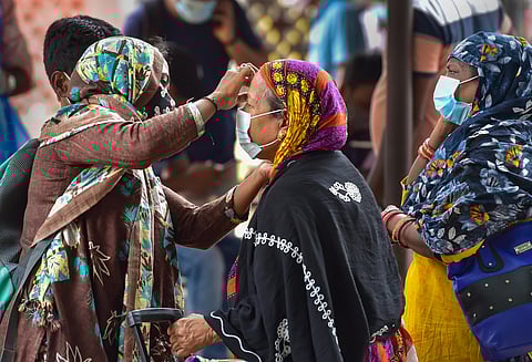 A woman helps an old lady to wear face mask at Bengaluru City Railway Station amid surge in coronavirus cases (Photo | PTI)