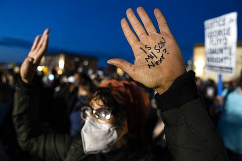A demonstrator's hands are raised, one with a message, as law enforcement officers are stationed behind a perimeter security fence, during a protest over the fatal shooting of Daunte Wright. | AP