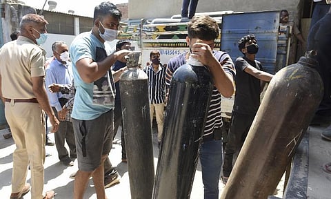 Family members of COVID-19 patient carry a cylinder after refilling it with medical oxygen, outside an oxygen filling centre (Photo | PTI)