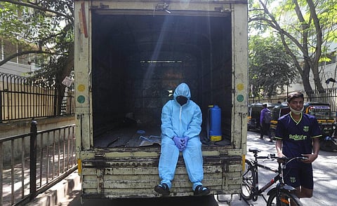 A civic worker rest on the back of a vehicle after sanitizing a building in Mumbai. (Photo | AP)