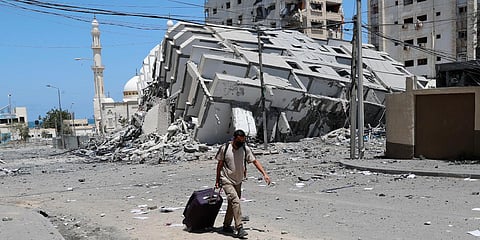 A man pulls his luggage while passing the rubble of a destroyed building which was hit by Israeli airstrikes, in Gaza City. (Photo| AP)