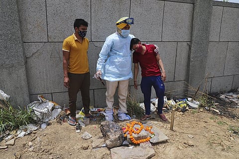 The caretaker of crematorium, center, tries to console a man who lost his five months old child to COVID-19 as they perform a post burial ritual at the Seemapuri crematorium in New Delhi. (Photo | AP)