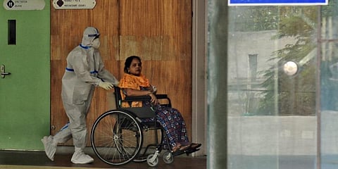 medic pushes a COVID-19 patient on a wheel-chair at Yamuna Sports Complex Covid Centre in New Delhi. (Photo | PTI)
