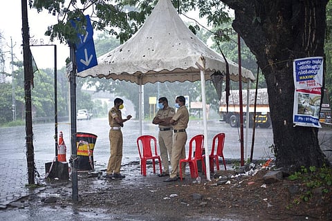 Policemen enforcing a lockdown to curb the spread of coronavirus stand beneath a rain shelter (Photo | AP)