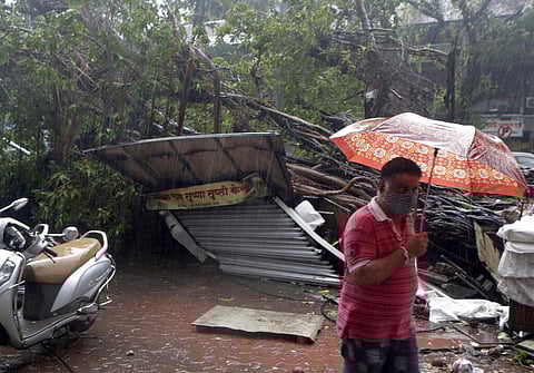 A man walks past a roadside shop that was damaged after a tree fell on it during a heavy rain in Mumbai. (Photo | AP)