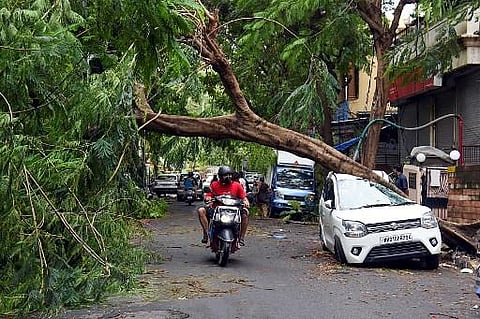 A motorist rides past a damaged car at a street in Mumbai on May 18, 2021. (Photo | AFP)