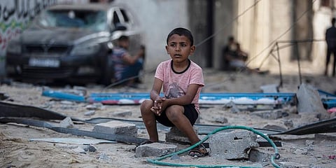 A Palestinian boy sits looking at others inspecting the damage of their shops following Israeli airstrikes on Jabaliya refugee camp, northern Gaza Strip. (Photo | AP)