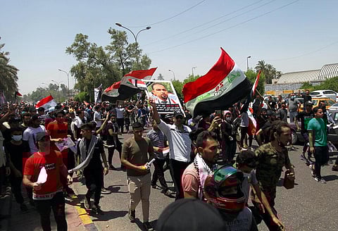 Anti-government protesters chant slogans as they hold posters of slain activist Ehab Wazni outside the Green Zone (Photo | AP)