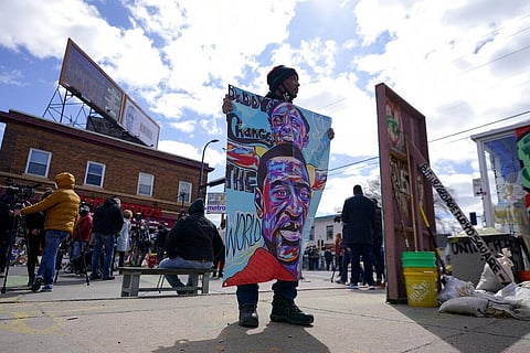 - In this Wednesday, April 21, 2021, file photo, a man holds a sign at George Floyd Square, in Minneapolis. (Photo | AP)