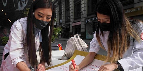 Dr. Michelle Lee (L) a radiology resident, and Ida Chen (R) a physician assistant student, prepare posters they carry at rallies protesting anti-Asian hate in New York's Chinatown. (Photo | AP)