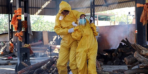 Family members wearing a PPE kit perform the last rites of the COVID19 people at cremation ground in Jammu. (Photo| ANI)