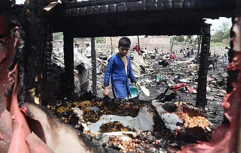 A boy seen collecting remains after a major fire destroyed about 50 shanties in the Rohingya Refugee Camp near Kalindi Kunj in New Delhi on Sunday. (Photo | Parveen Negi, EPS)