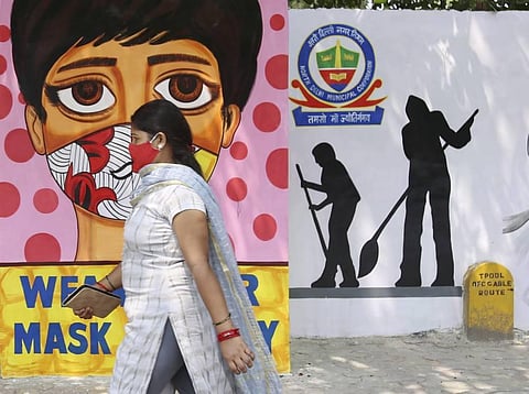 A woman walks past a wall mural on raising awareness about wearing facemasks, amid the ongoing COVID-19 pandemic in New Delhi. (File Photo | PTI)