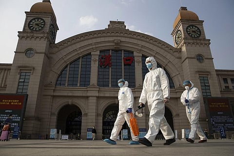 Workers in protective overalls walk past the Hankou railway station in Wuhan in central China's Hubei province. (Photo | AP)