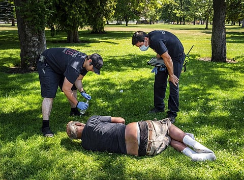 With the temperature well over 100 degrees, firefighters assigned to the Alternative Response Unit of Station 1, check on the welfare of a man in Mission Park in Spokane (Photo |AP)