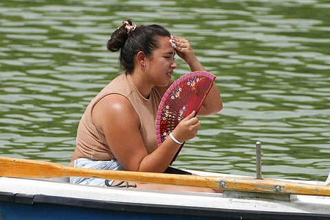 A woman mops her brow while fanning herself on a rowing boat in the Retiro park in Madrid, Spain. (Photo | AP)
