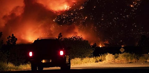 A motorist watches from a pullout on the Trans-Canada Highway as a wildfire burns on the side of a mountain in Lytton, B.C., Thursday, July 1, 2021. (Photo | AP)