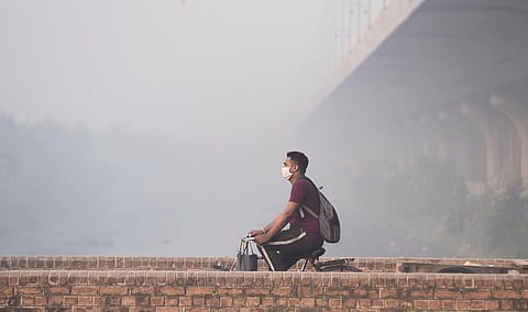 A man wearing a facemask rides his bicycle along a street in Delhi. (File | Parveen Negi, EPS)